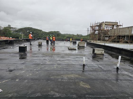Equipo de IIECA trabajando en techo con membrana asfáltica bajo lluvia